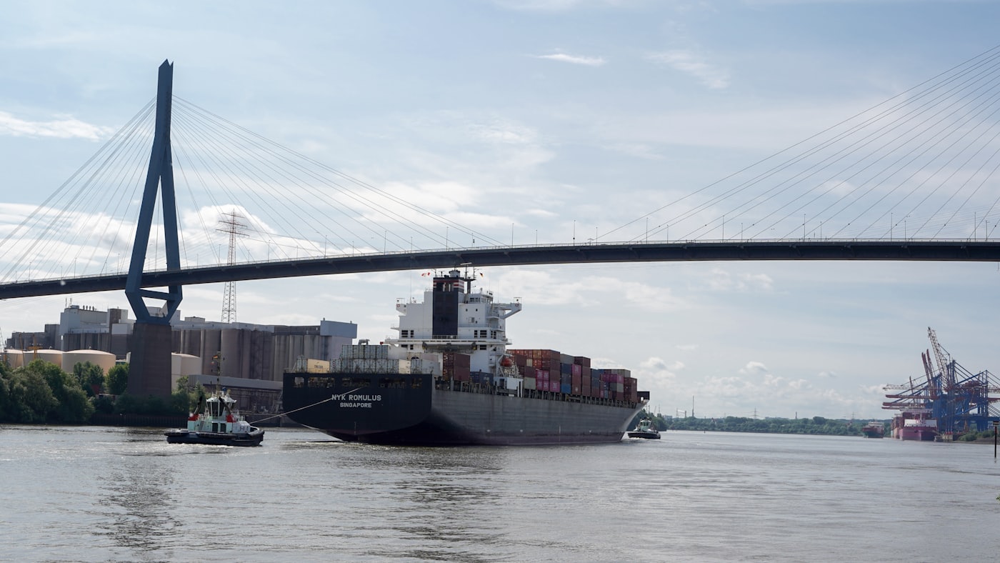 Een groot containerschip vaart onder een brug een haven binnen